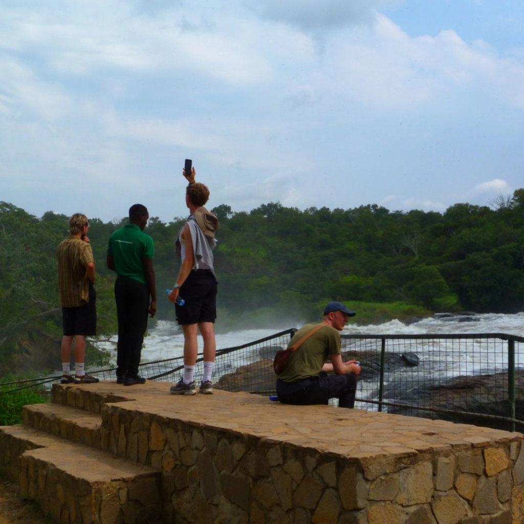 Visitors standing at a stone viewpoint looking toward a river and falls