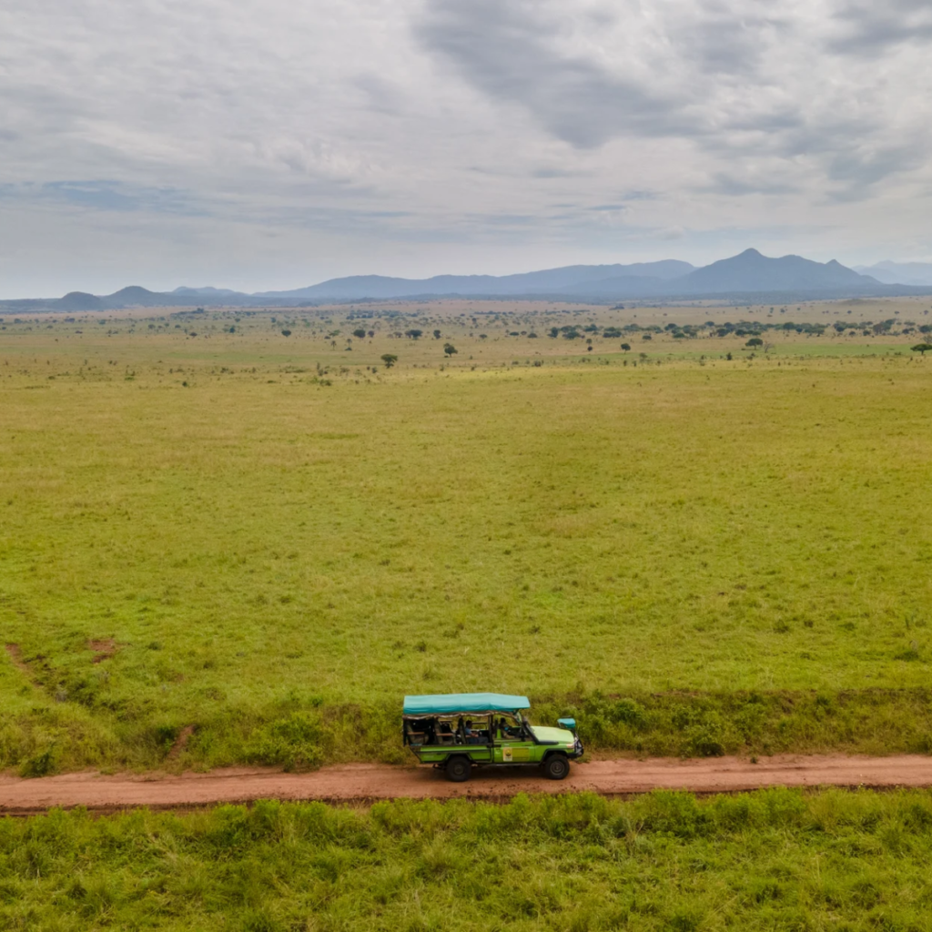 Aerial view of a safari vehicle on a red track crossing green plains toward distant hills