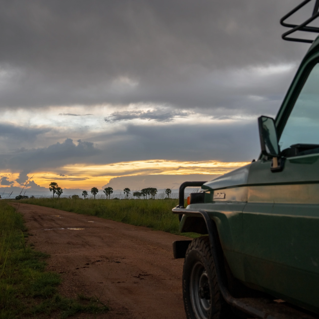 A safari vehicle parked on a dirt road beneath a stormy dusk sky